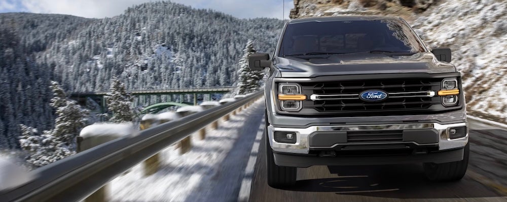 A gray 2026 Ford F-150 pickup truck driving down a snowy mountain road