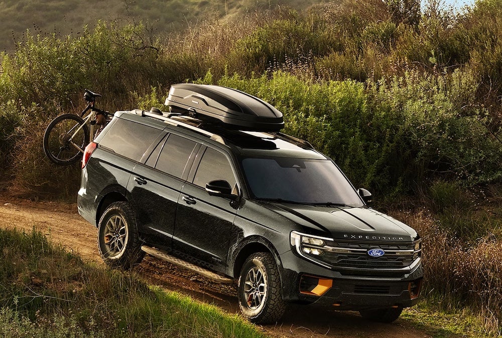 A black 2027 Ford Expedition SUV with a cargo box driving down a dirt trail