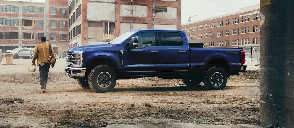 A person walking past a blue 2026 Ford Super Duty truck at a construction site