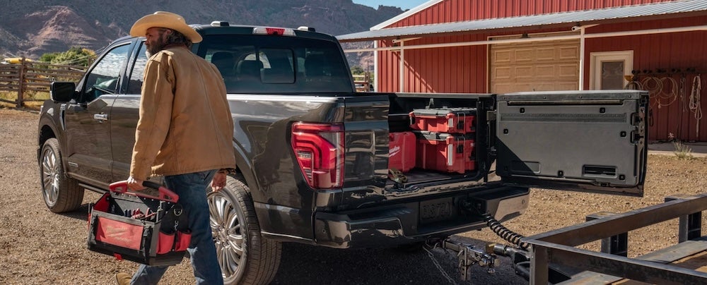 A man carrying a tool kit beside a gray 2026 Ford F-150 pickup truck at a ranch